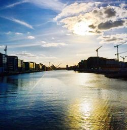 River by cityscape against sky during sunset