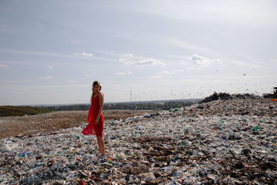 Young woman standing on garbage against sky