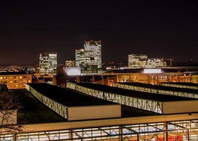 Illuminated bridge by buildings against sky at night