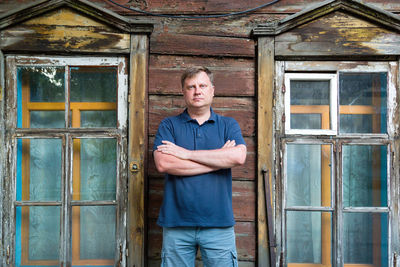 An adult man stands at wooden abandoned building.