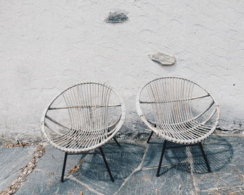 Empty papasan chairs on footpath by white wall