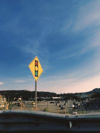 Road sign by street against blue sky