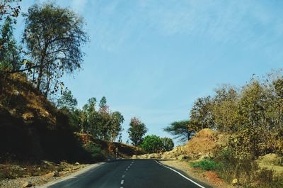 Country road amidst trees against sky