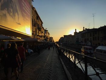 People on railroad tracks against sky during sunset