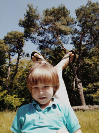 Boy sitting on father laps in park against trees