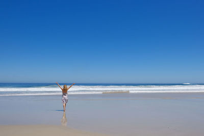 Woman walking at beach against clear blue sky