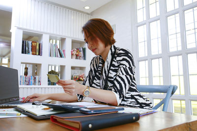 Businesswoman using credit card and laptop at desk in office