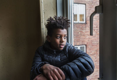 Portrait of young man looking away while sitting against window