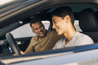Happy young man learning to drive while sitting with father in car