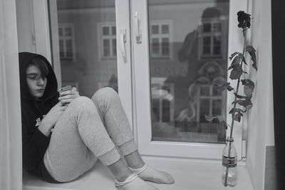 Girl using mobile phone while sitting on window sill