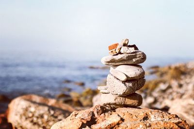 Pebbles stacked on rock at beach against clear sky