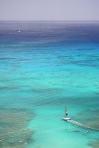 Coloful sailboat, sailing past surfers in turquoise waters of waikiki into the ocean on oahu, hawaii