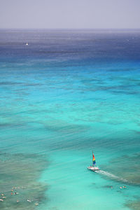 Coloful sailboat, sailing past surfers in turquoise waters of waikiki into the ocean on oahu, hawaii