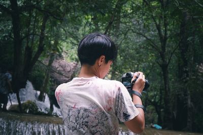 Rear view of woman photographing against trees