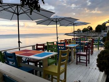 Chairs and tables at restaurant by sea against sky during sunset