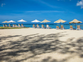 Lounge chairs on beach against blue sky