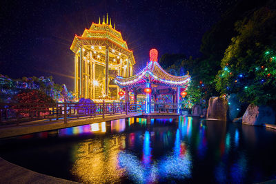 Illuminated building by river against sky at night