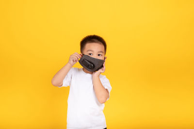 Portrait of boy holding camera against yellow background