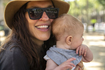 Portrait of smiling woman wearing sunglasses while carrying daughter