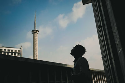 Low angle view of man standing by building against sky