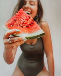 Smiling woman holding watermelon standing against wall