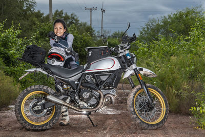 Woman posing behind her scrambler style motorcycle on dirt road