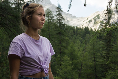 Thoughtful young woman standing against trees in forest