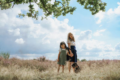 Rear view of two girls standing on field against sky with holding hands