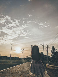 Rear view of woman with dog against sky during sunset