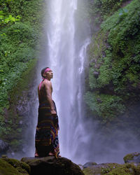 Man standing amidst rocks against waterfall