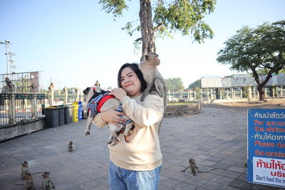 Portrait of smiling woman with dog and monkey standing in city