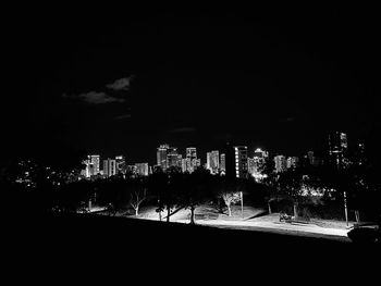 Silhouette trees by illuminated buildings against sky at night