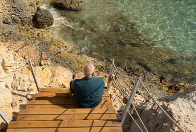 High angle view of man sitting on steps at shore