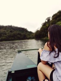 Rear view of woman sitting on river against sky