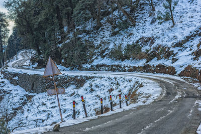 Snow covered road by trees against mountain