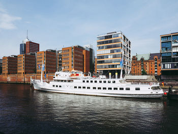 Boats on river by buildings in city against sky