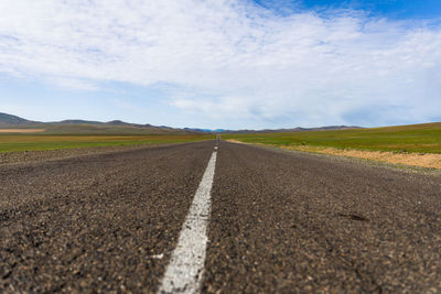 Surface level of road amidst field against sky