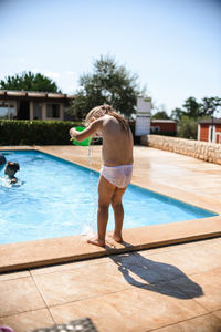 Little girl swimming in the pool. watering herself from a bucket