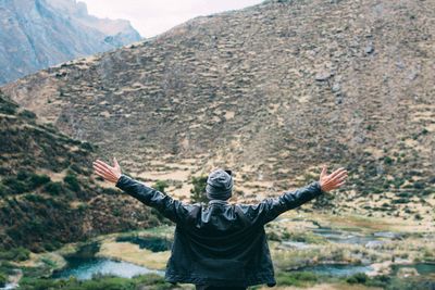 Rear view of man with arms outstretched standing against mountain