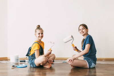 A girl with her sister in bright blue and yellow clothes helps to paint the walls in her room white.