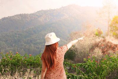 Rear view of woman pointing at trees while standing against mountains