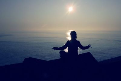 Silhouette man sitting on sea against sky during sunset