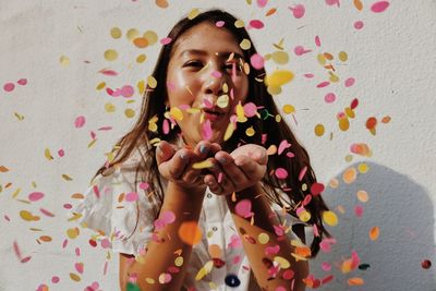 Young woman blowing confetti against wall