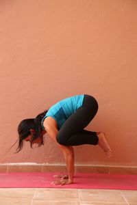 Young woman in crow pose by wall