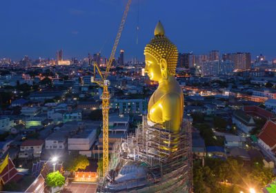 Illuminated statue amidst buildings in city against sky