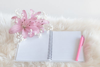 Close-up of blank book with pen and pink flower on white rug