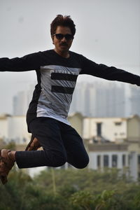 Full length of young man jumping outdoors, high jump joying bilding bihands lage on air jump