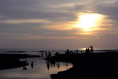 Silhouette people on beach against sky during sunset