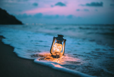 Illuminated lamp in sea against sky at sunset