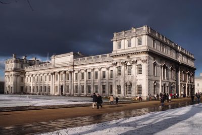 People in front of historical building against cloudy sky